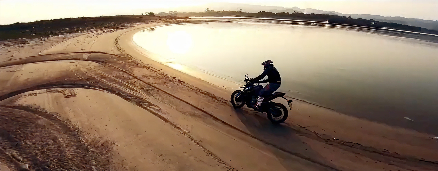 Zontes motos en Argentina - Zontes 200U circulando sobre arena junto al agua con conductor equipado en una toma amplia.