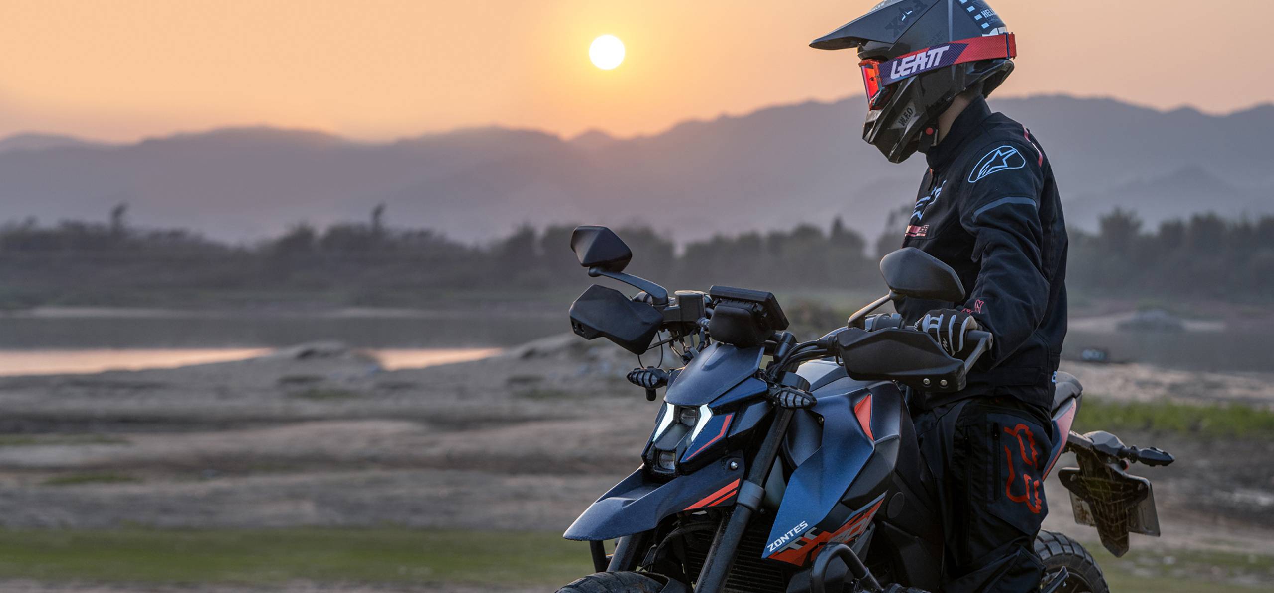 Zontes motos en Argentina - Moto Zontes 200U con piloto detenido en un entorno natural con sol bajo y montañas al fondo. Zontes motos en Argentina - Zontes 200U detenida con conductor equipado frente a un paisaje abierto al atardecer.