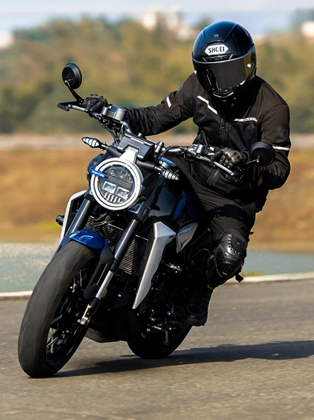 Zontes motos en Argentina - Zontes 350GK en curva con conductor vestido de negro y faro redondo encendido.