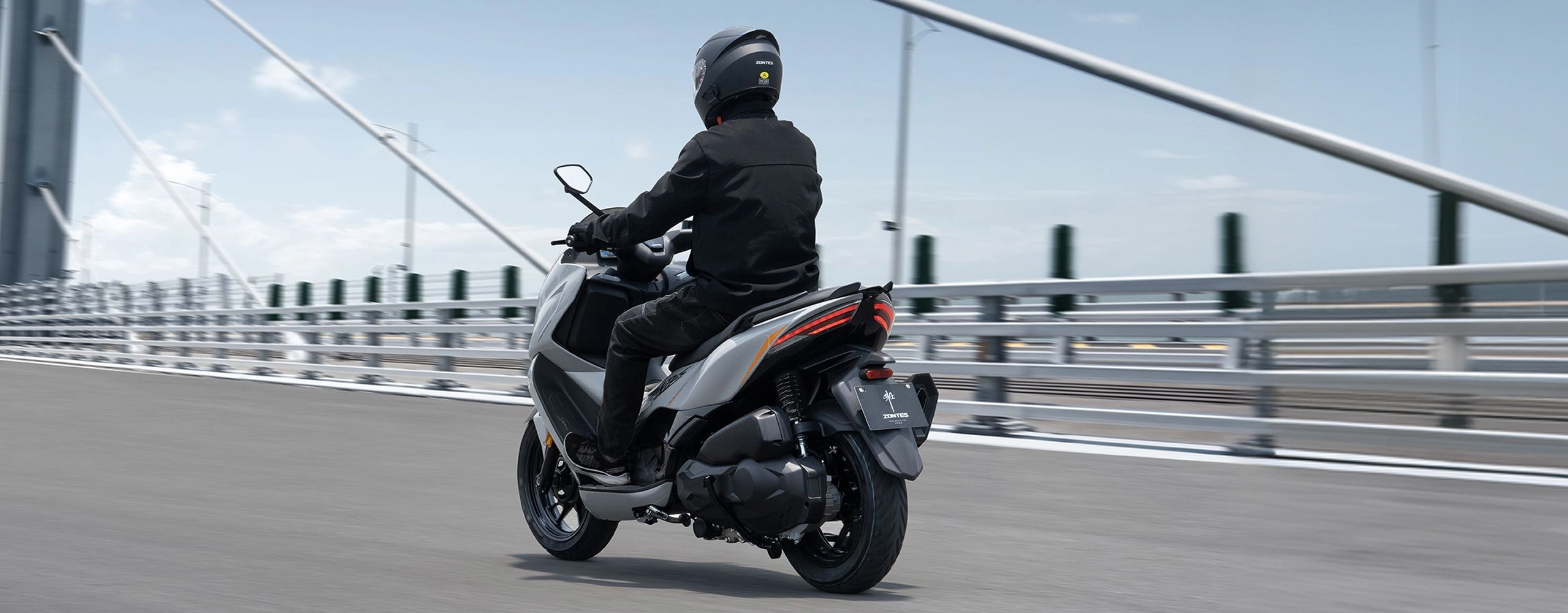Zontes motos en Argentina - Scooter 368D circulando con sector trasero visible, suspension lateral y cola estilizada. Zontes motos en Argentina - Zontes 368D en marcha visto desde atras con conductor y luz posterior encendida sobre un puente urbano.